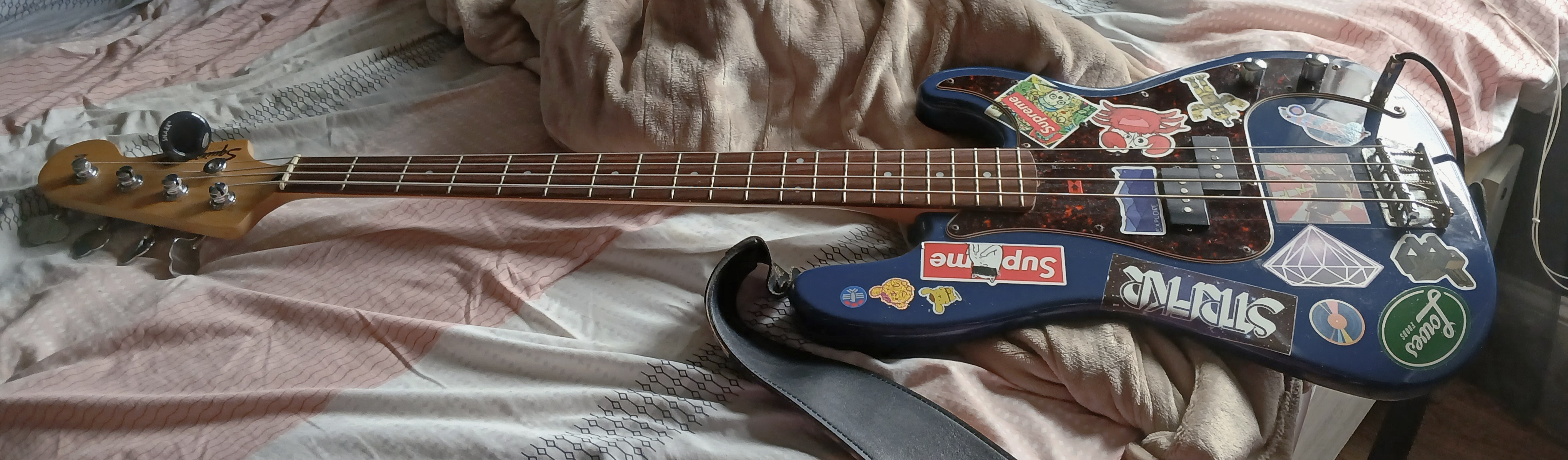 A blue 4 string bass guitar. It has a wooden neck and head, with a blue body and red scratch plate. 
 It is covered in stickers.